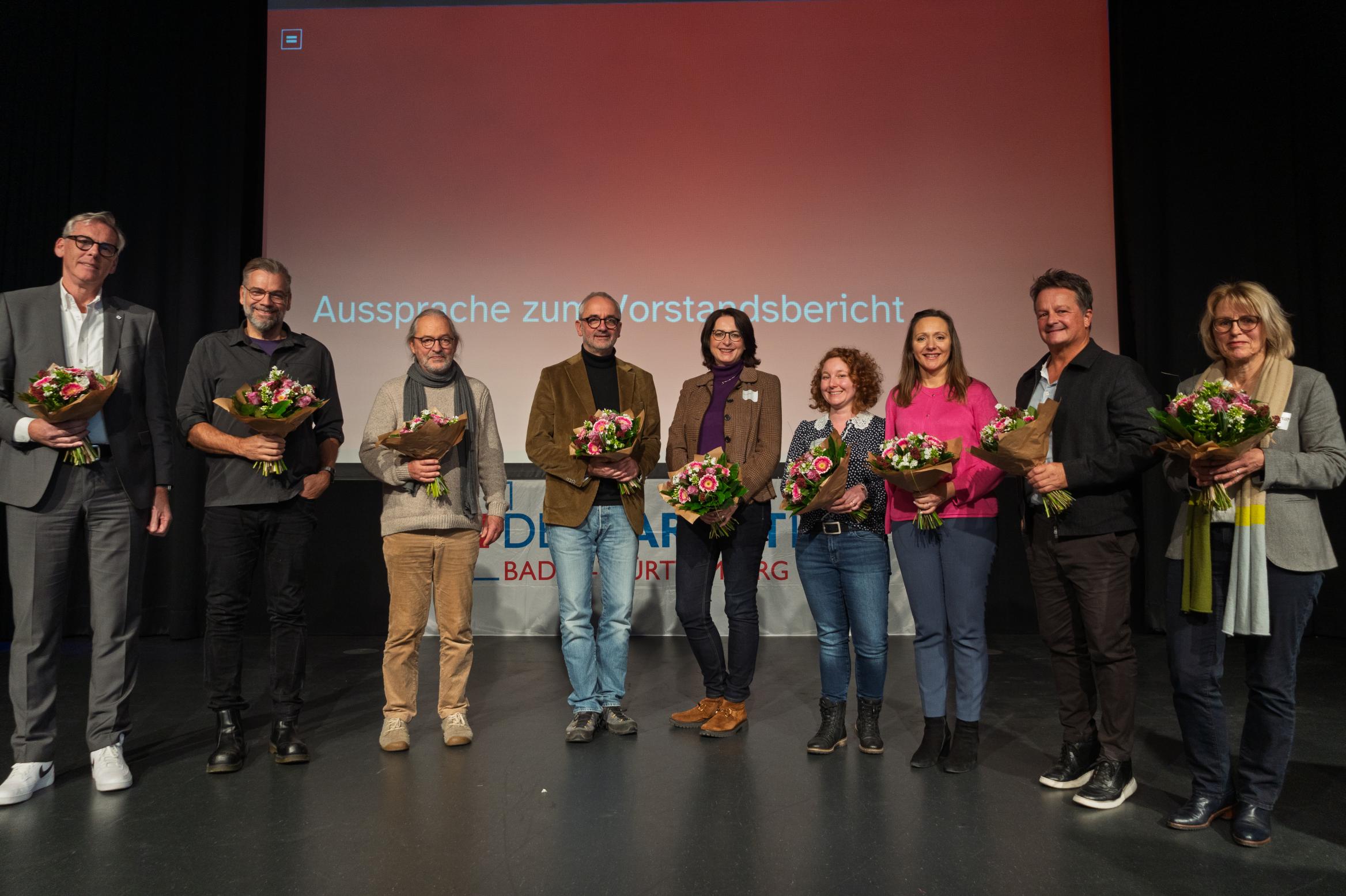 mehrere Personen mit Blumensträußen stehen auf einer Bühne
