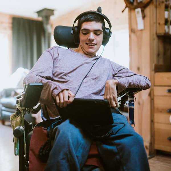 junger Mann im Rollstuhl hört mit Kopfhörern Musik