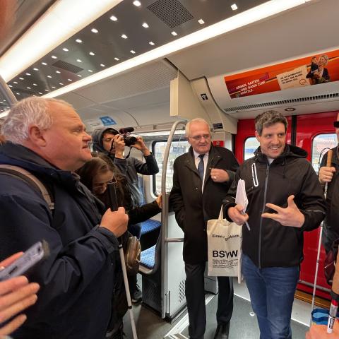 Personen stehen in der S-Bahn und diskutieren. Ein Kameramann filmt den Austausch