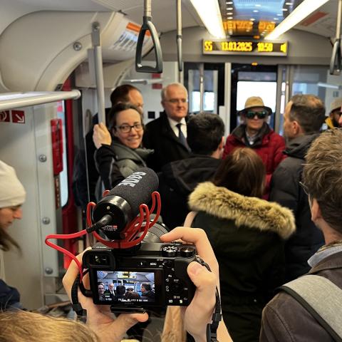 Personen stehen in der S-Bahn und diskutieren. Ein Kameramann filmt den Austausch