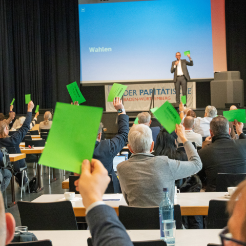 grüne Wahlzettel in einem Raum werden hochgehalten