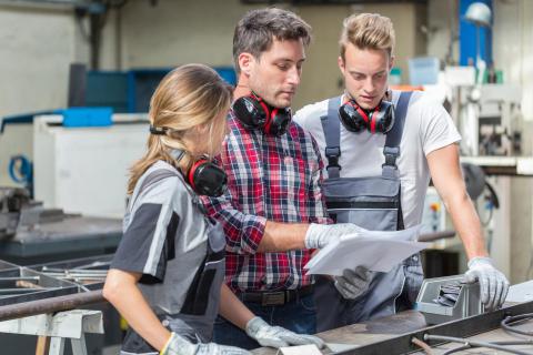 2 Auszubildende an einer Maschine mit einem Ausbilder