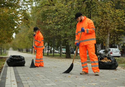 Menschen in oranger Arbeitskleidung fegen die Straße