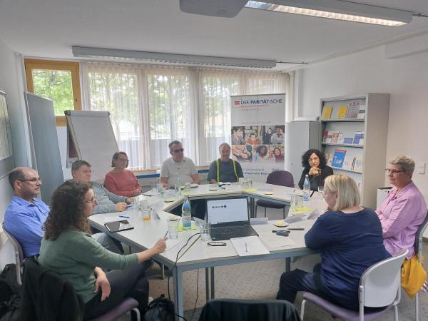 mehrere Personen sitzen im Kreis an einem runden Tisch