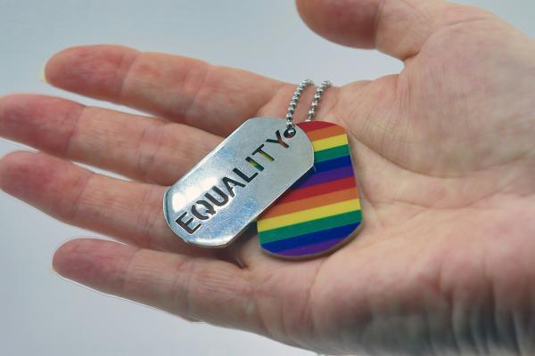 eine Hand hält einen Regenbofgen anhänger und eine Plakette mit Equality