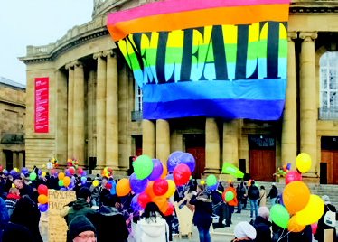 Regenbogenflagge weht vor der Staatsoper in Stuttgart. eine Demo davor.