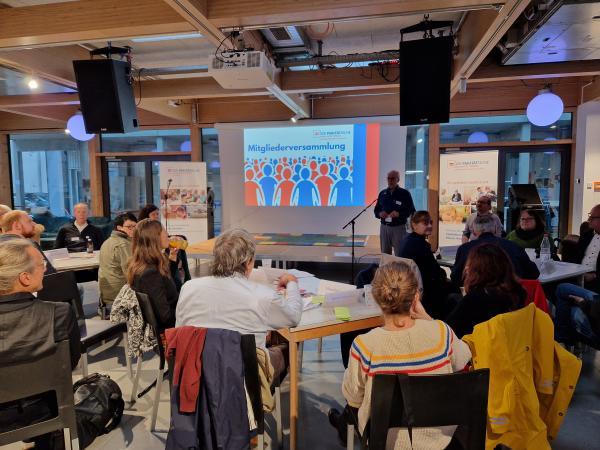 großer Raum mit einer Leinwand und vielen Menschen von hinten