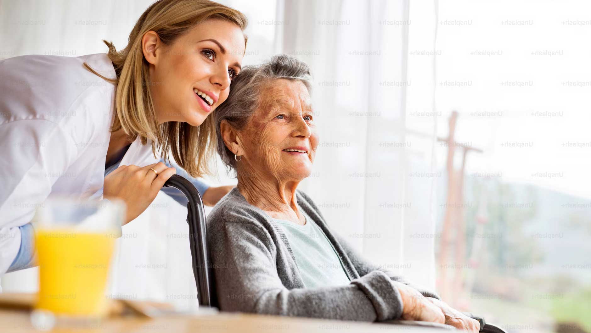 Pflegekraft steht hinter einer älteren Dame im Rollstuhl