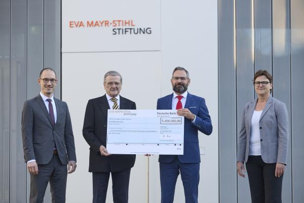 Drei Männer und eine Frau stehen nebeneinander mit Scheck in der Hand