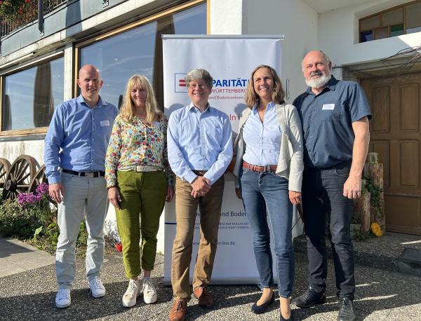 3 Männer und 2 Frauen vor dem Paritätischen Logo