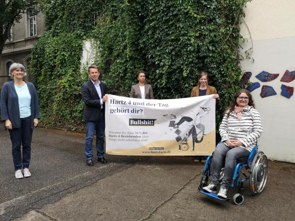 4 Personen und eine Frau im Rollstul vor dem Plakat HartzFacts