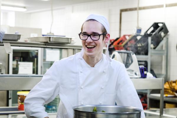 Junger Mann in Kochkleidung in Großküche