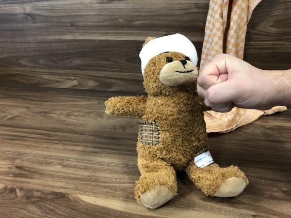 Verletzter Teddybär mit vebundemKopf und Pflaster auf dem Oberschenkel