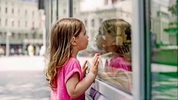 Ein junges Mädchen schaut ins Fenster und spiegelt sich