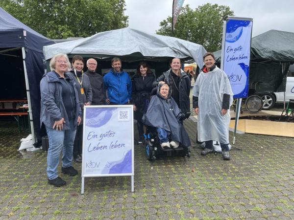 Männer und Frauen stehen im Halbkreis vor Pavillon