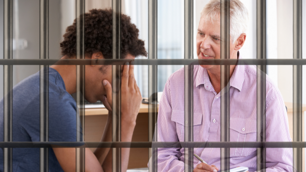 Mann mit schwarzen Locken sitzt hinter Gittern und wird von mann beraten