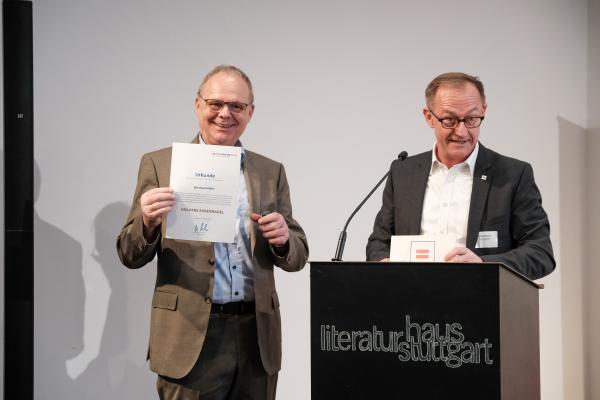 Herr Müller und Herr Hartmann am Rednerpult. Herr Müller zeigt seine Ehrenurkunde