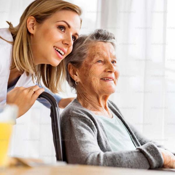 Pflegekraft steht hinter einer älteren Dame im Rollstuhl